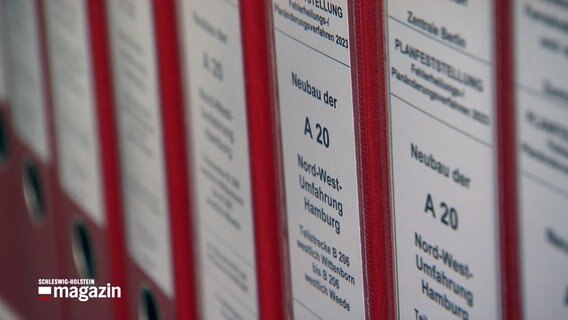 Ein roter Aktenordner mit der Bezeichnung "Neubau der A20" steht in einem Regal mit anderen Aktenordnern. © NDR 
